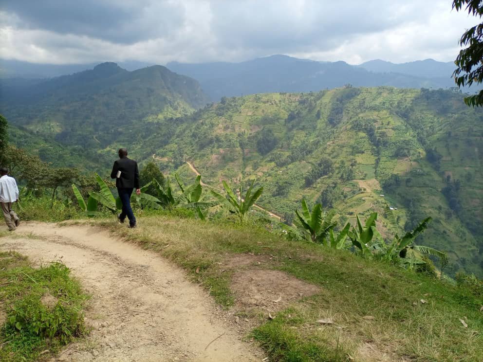 A CGALU team member walking a dirt path toward a remote village in the hills of Uganda